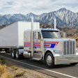 White Peterbilt semi-truck with red and blue stripes driving on desert highway with snow-capped mountains in background