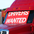 Red commercial truck with 'Drivers Wanted' recruitment sign on cabin window