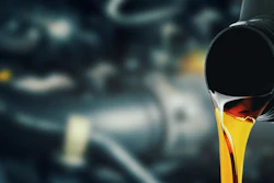 Golden motor oil pouring from a black container against an engine background