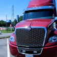 Red Volvo semi-truck parked on highway with white tanker trailer and blue sky