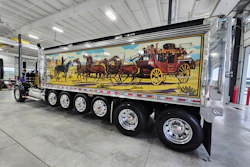 Large commercial truck with colorful stagecoach and horses mural painted on trailer side in industrial warehouse setting