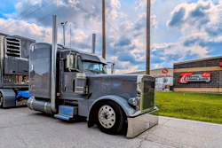 Black and blue Peterbilt semi-truck with refrigerated trailer parked at industrial facility under cloudy sky