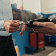 Two people completing a contactless payment transaction with a portable card reader in an industrial warehouse setting.