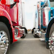 Red and blue commercial semi-trucks parked side by side with polished chrome wheels and fuel tanks