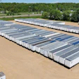 Aerial view of storage facility with rows of white and gray trailer units parked on dirt ground surrounded by trees