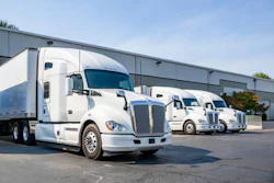 Fleet of white commercial semi-trucks parked outside industrial warehouse facility