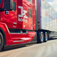 Red Kodiak semi-truck with trailer driving on highway under blue sky