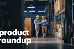 Two warehouse workers in hard hats reviewing inventory among storage boxes and shelving in an industrial facility