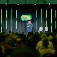 Speaker presenting at 'Go Grow Thrive' conference on stage with audience and green neon lighting