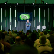 Speaker presenting at 'Go Grow Thrive' conference on stage with audience and green neon lighting