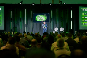 Speaker presenting at 'Go Grow Thrive' conference on stage with audience and green neon lighting