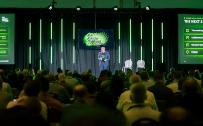 Speaker presenting at 'Go Grow Thrive' conference on stage with audience and green neon lighting