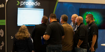 Group of professionals gathered at Procede booth examining monitor display during tech conference
