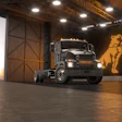 Black Mack semi-truck with illuminated grille displayed in modern industrial showroom with amber digital signage