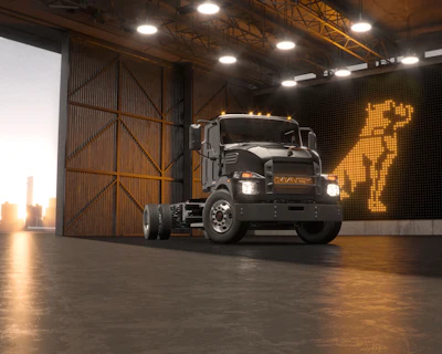 Black Mack semi-truck with illuminated grille displayed in modern industrial showroom with amber digital signage