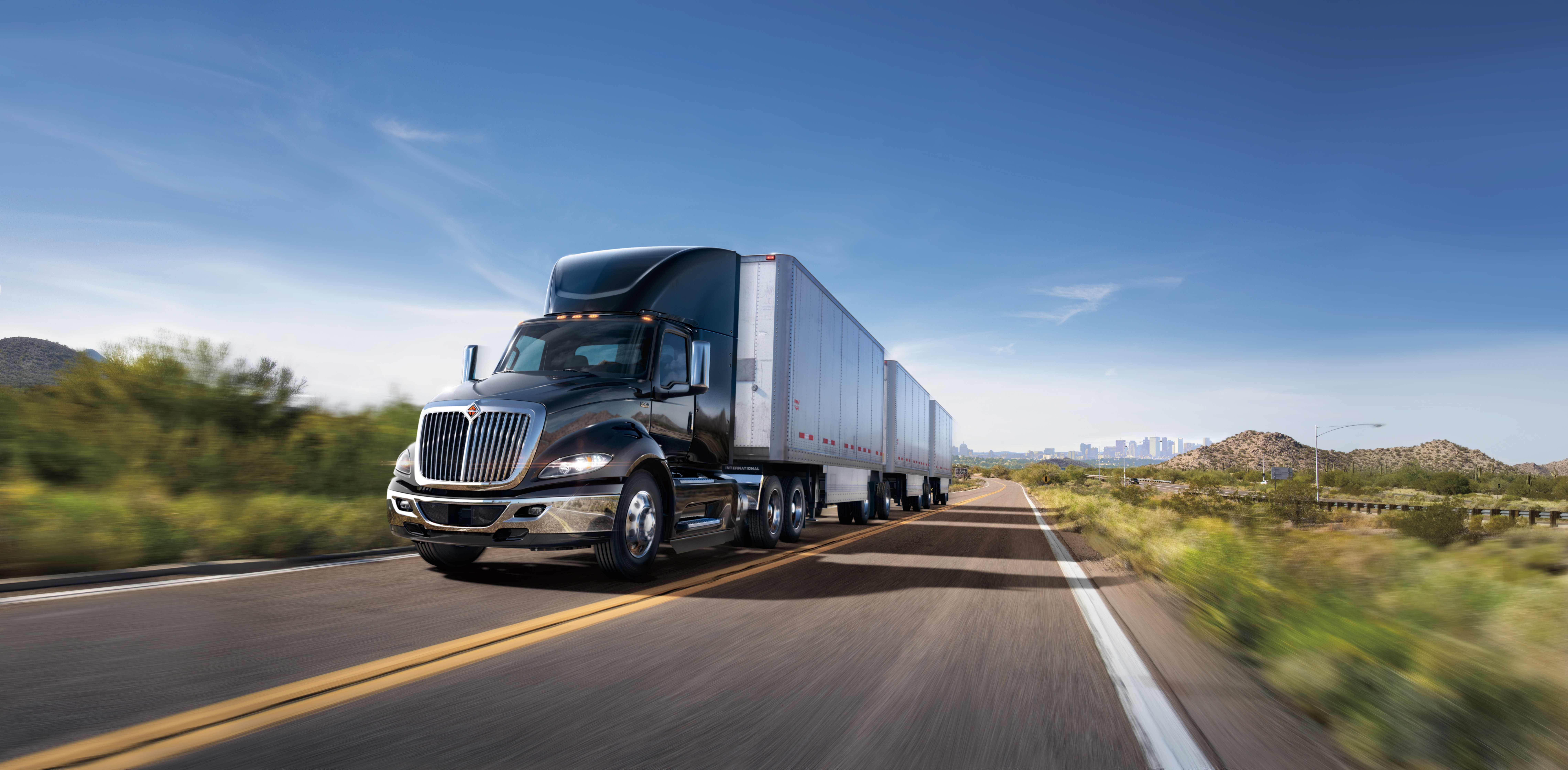 Semi-truck with cargo trailer driving on highway through desert landscape under clear blue sky