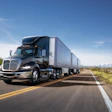 Semi-truck with cargo trailer driving on highway through desert landscape under clear blue sky