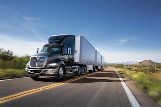 Semi-truck with cargo trailer driving on highway through desert landscape under clear blue sky