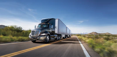 Semi-truck with cargo trailer driving on highway through desert landscape under clear blue sky