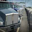 Row of International commercial trucks parked at a dealership with palm trees and industrial facility in background