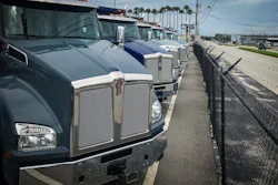 Row of International commercial trucks parked at a dealership with palm trees and industrial facility in background