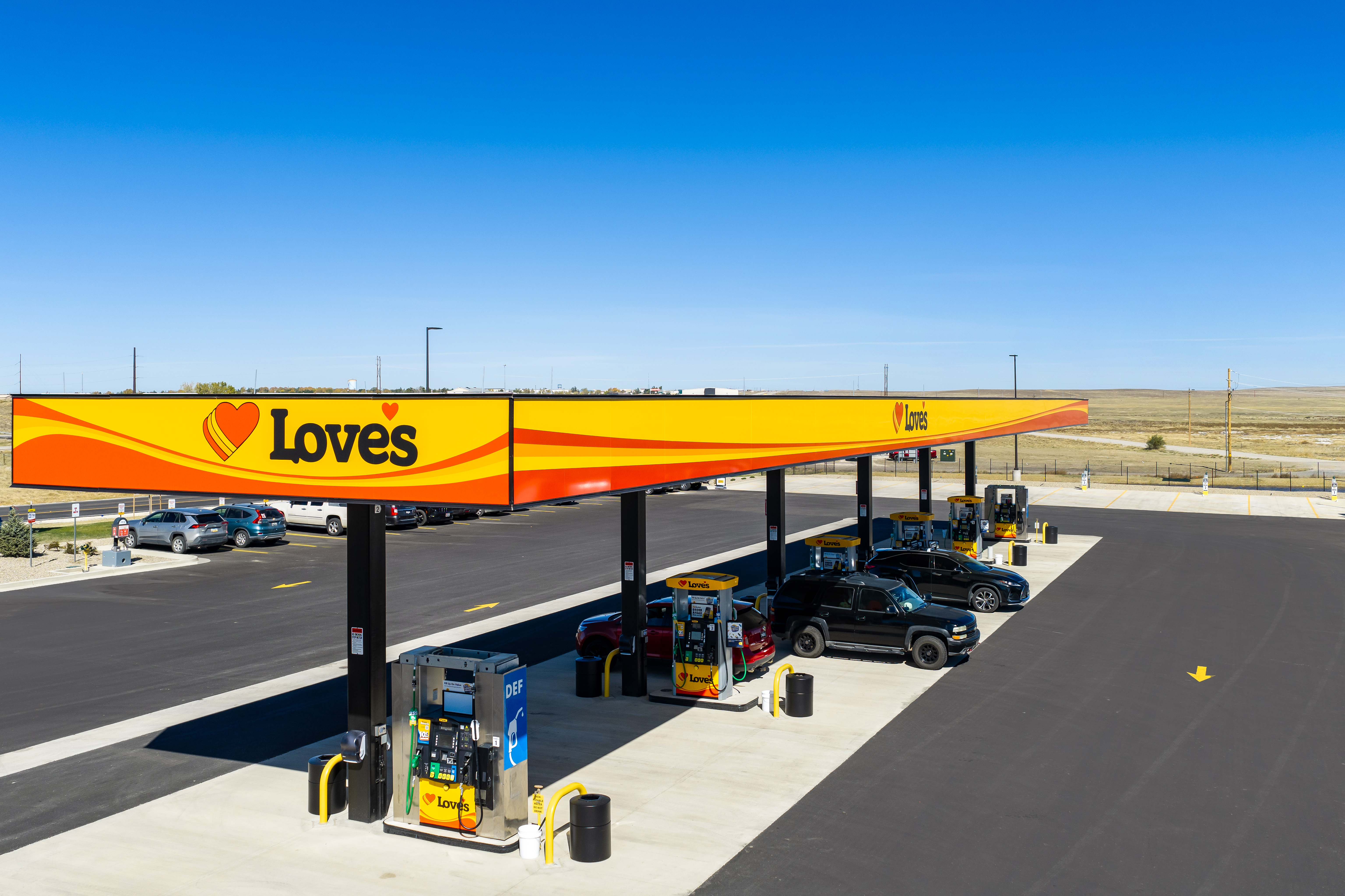 Love's Travel Stops gas station with yellow and red canopy, fuel pumps, and vehicles parked in an arid landscape.