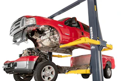 Two-post automotive lift holding damaged red pickup trucks in repair shop setting