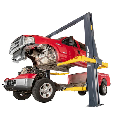 Two-post automotive lift holding damaged red pickup trucks in repair shop setting