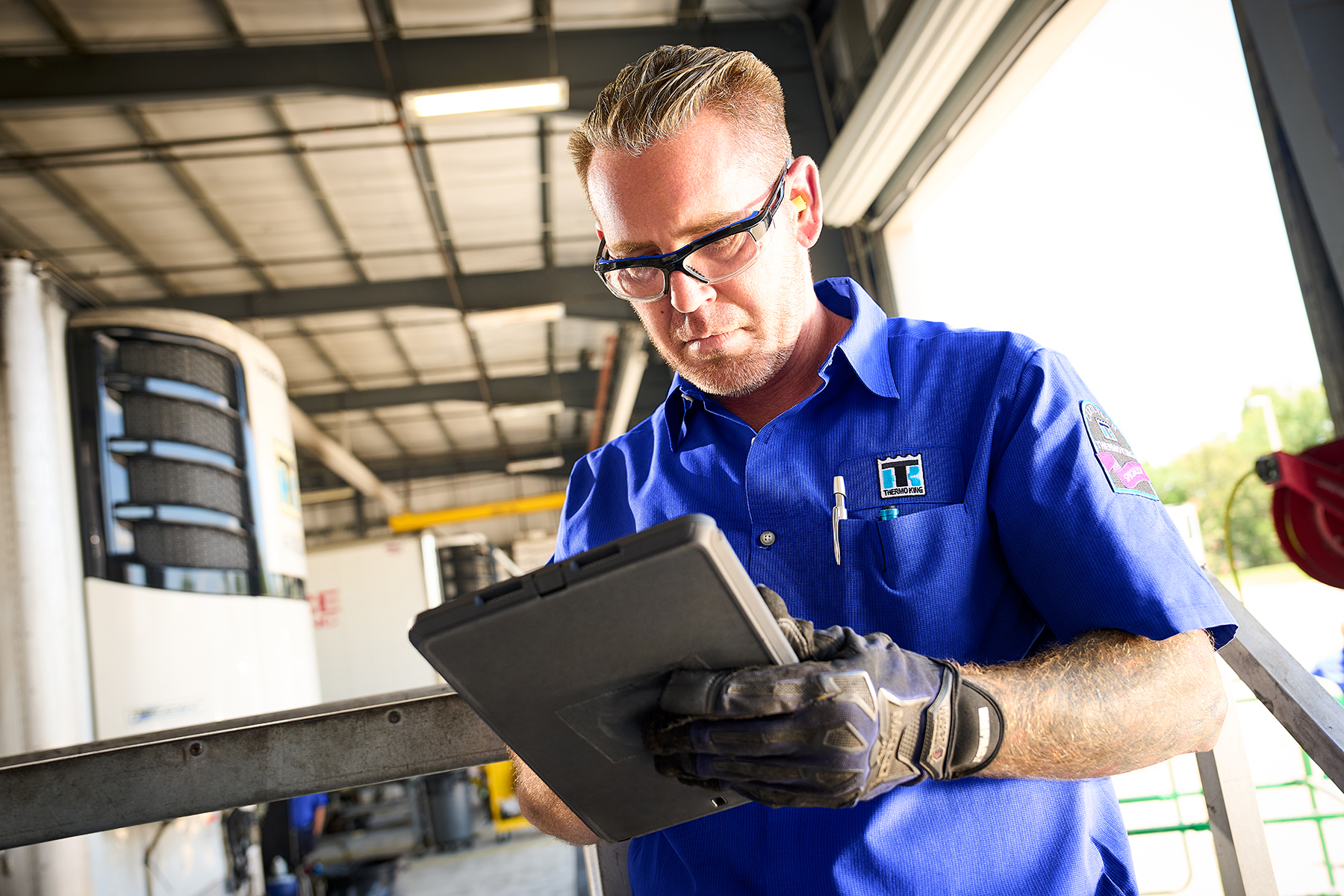 Technician in blue uniform examining tablet in industrial garage setting