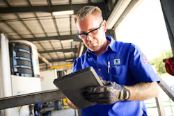 Technician in blue uniform examining tablet in industrial garage setting