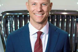 Professional headshot of a smiling man in navy blazer and burgundy tie against a blurred background
