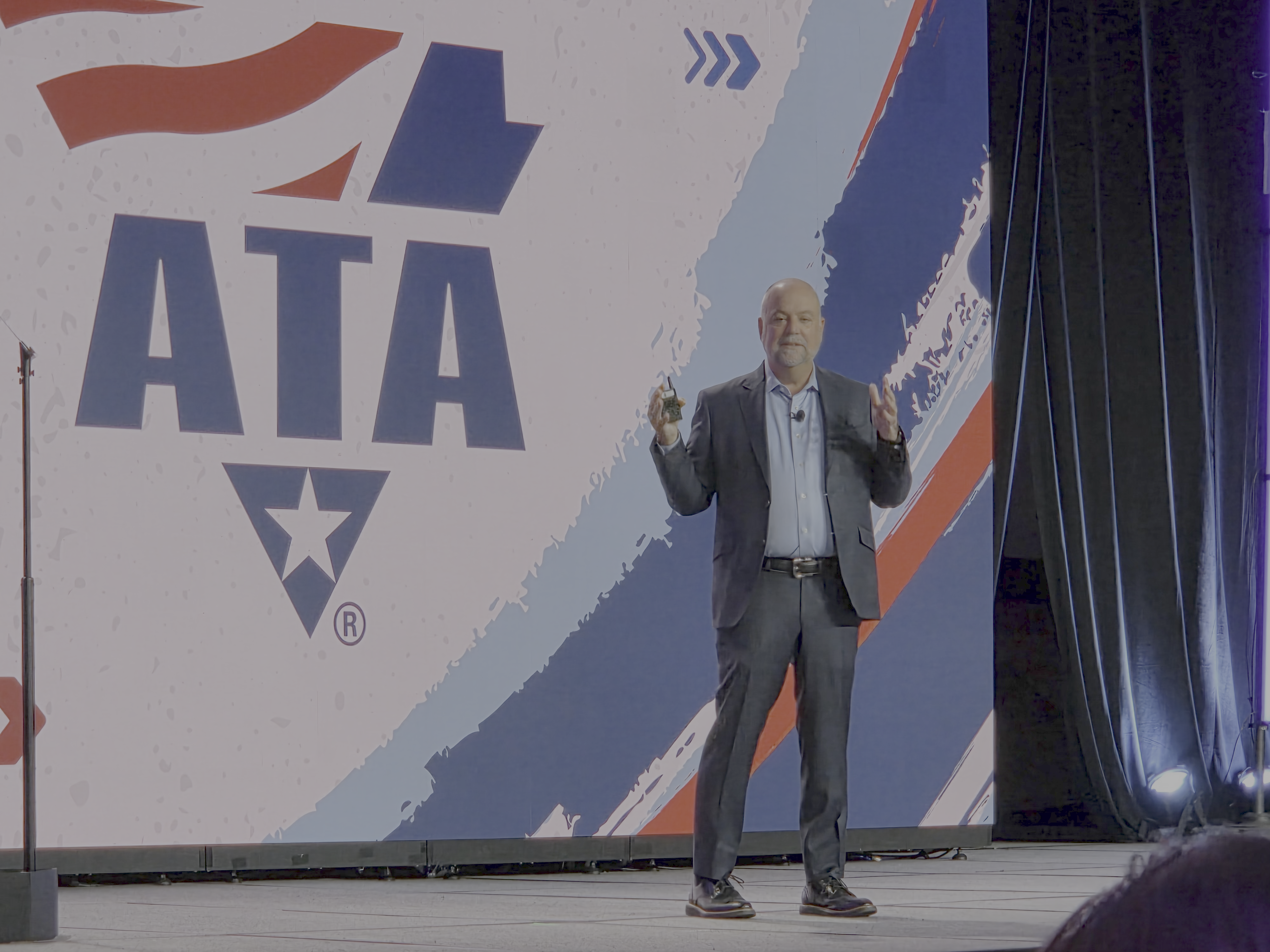 Professional speaker presenting at podium with ATA logo displayed on stage backdrop