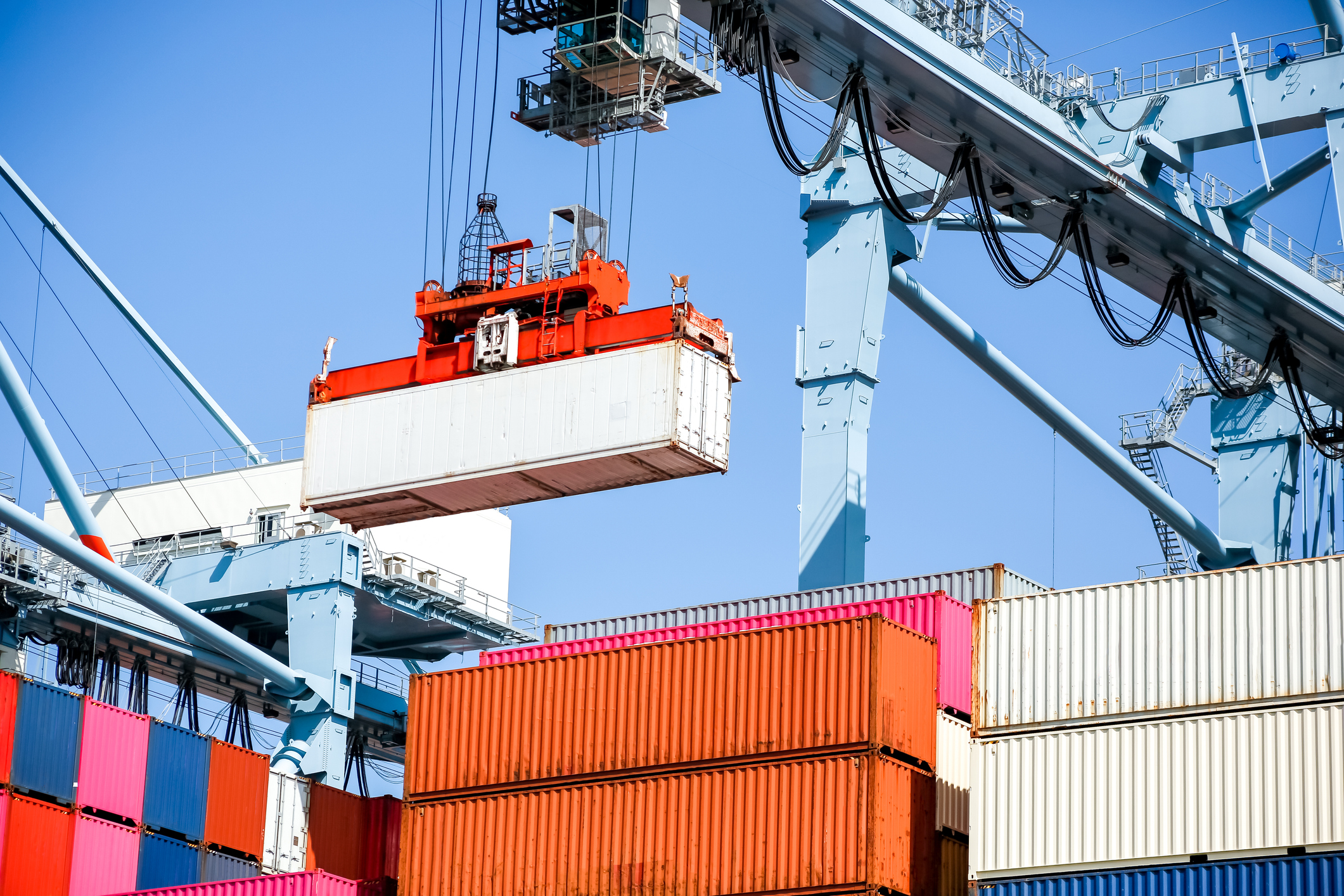Port cargo terminal with orange shipping containers and overhead gantry crane loading operations