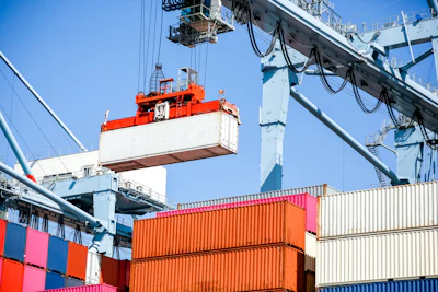 Port cargo terminal with orange shipping containers and overhead gantry crane loading operations