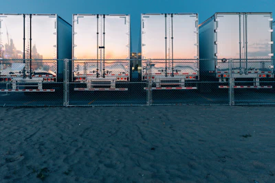 Row of industrial shipping containers at a waterfront dock with city skyline visible through open doors at sunset