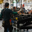 Factory workers assembling heavy machinery with chains and tools in an industrial manufacturing facility