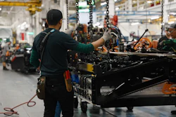 Factory workers assembling heavy machinery with chains and tools in an industrial manufacturing facility