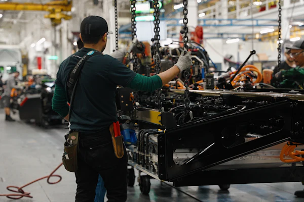 Factory workers assembling heavy machinery with chains and tools in an industrial manufacturing facility