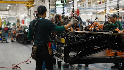 Factory workers assembling heavy machinery with chains and tools in an industrial manufacturing facility