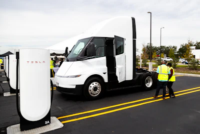 Tesla Semi truck charging at a Supercharger station with worker in safety vest
