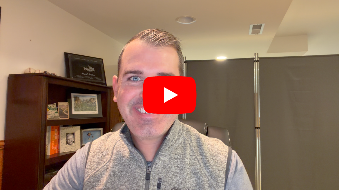Man in gray vest smiling at camera in office setting with YouTube play button overlay