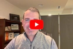 Man in gray vest smiling at camera in office setting with YouTube play button overlay