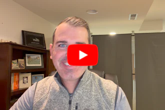 Man in gray vest smiling at camera in office setting with YouTube play button overlay