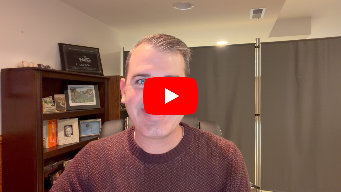 Man in burgundy sweater speaking to camera with YouTube play button overlay in office setting