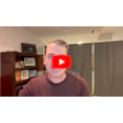 Man in burgundy sweater speaking to camera with YouTube play button overlay in office setting