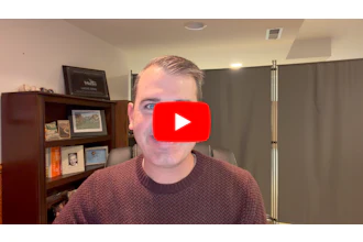 Man in burgundy sweater speaking to camera with YouTube play button overlay in office setting
