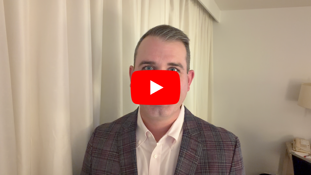 Professional man in plaid blazer with YouTube play button overlay indicating video content