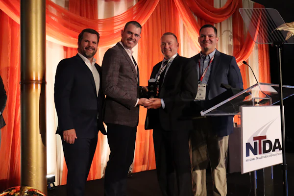 Four men in business suits stand together at NTDA event podium with red stage lighting, one holding an award