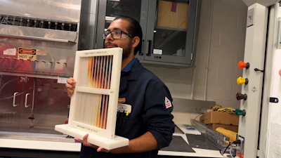 Technician holding a cream-colored air filter sample with brown gradient stripes in a laboratory setting