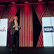Professional speaker presenting at corporate event with KEA Advisors branding displayed on large screens